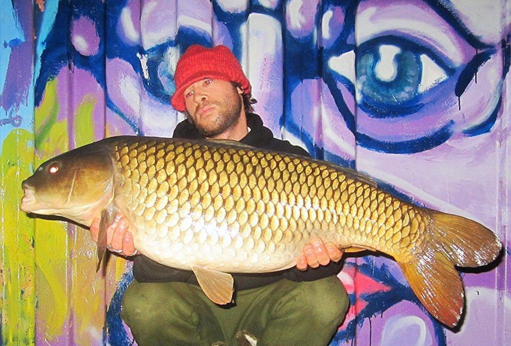 Sam holding big carp in front of graffiti