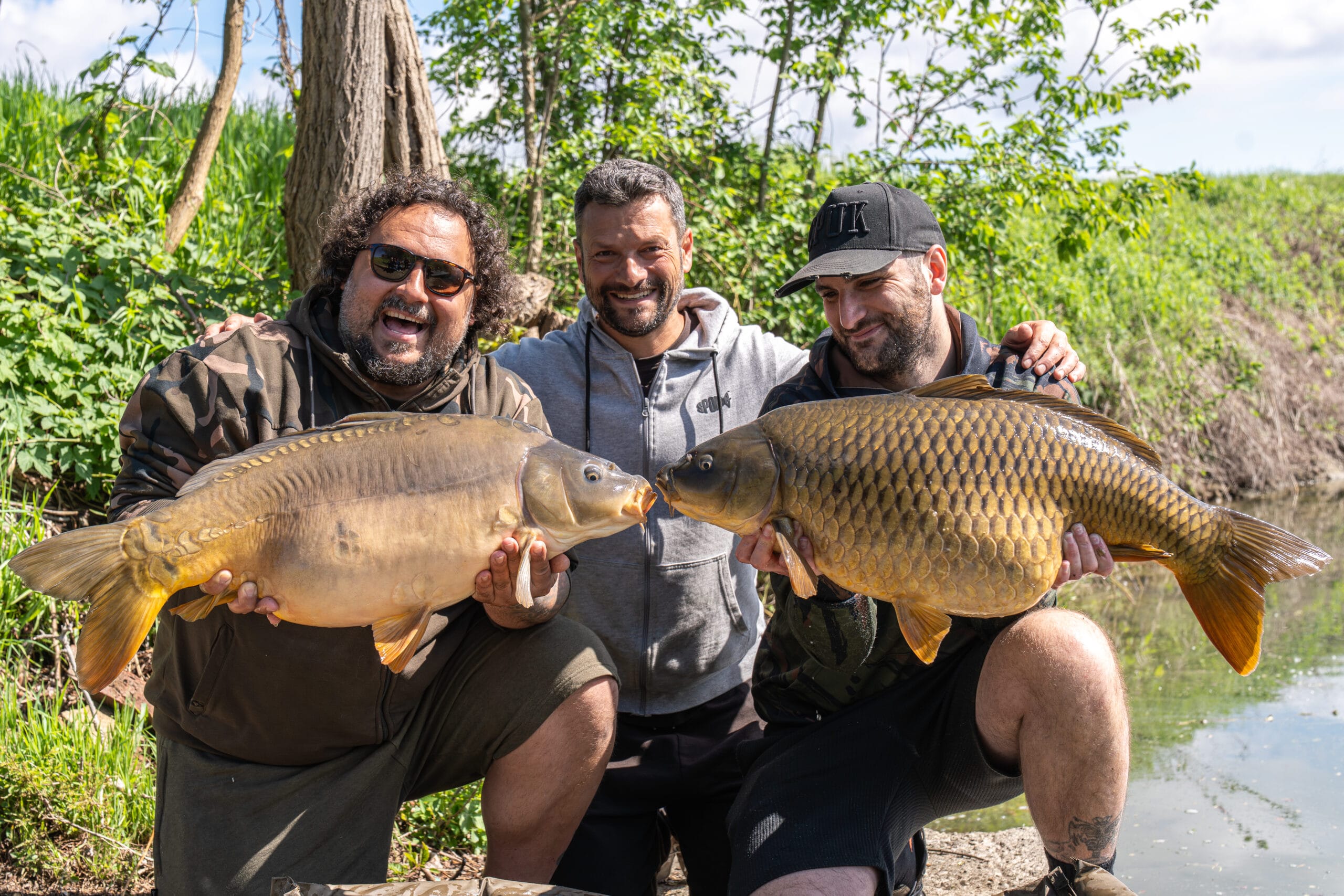 Three men with big carps by the riverbank.