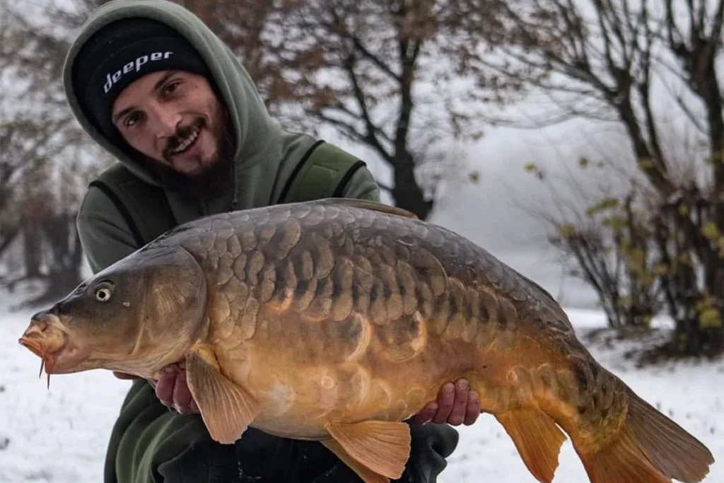 Person holding large carp in snowy landscape