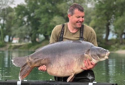 Man holding large fish near a lake.