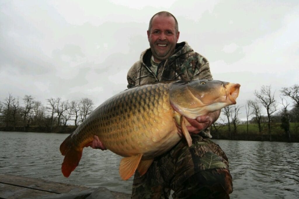 Angler holding large carp by a lake.