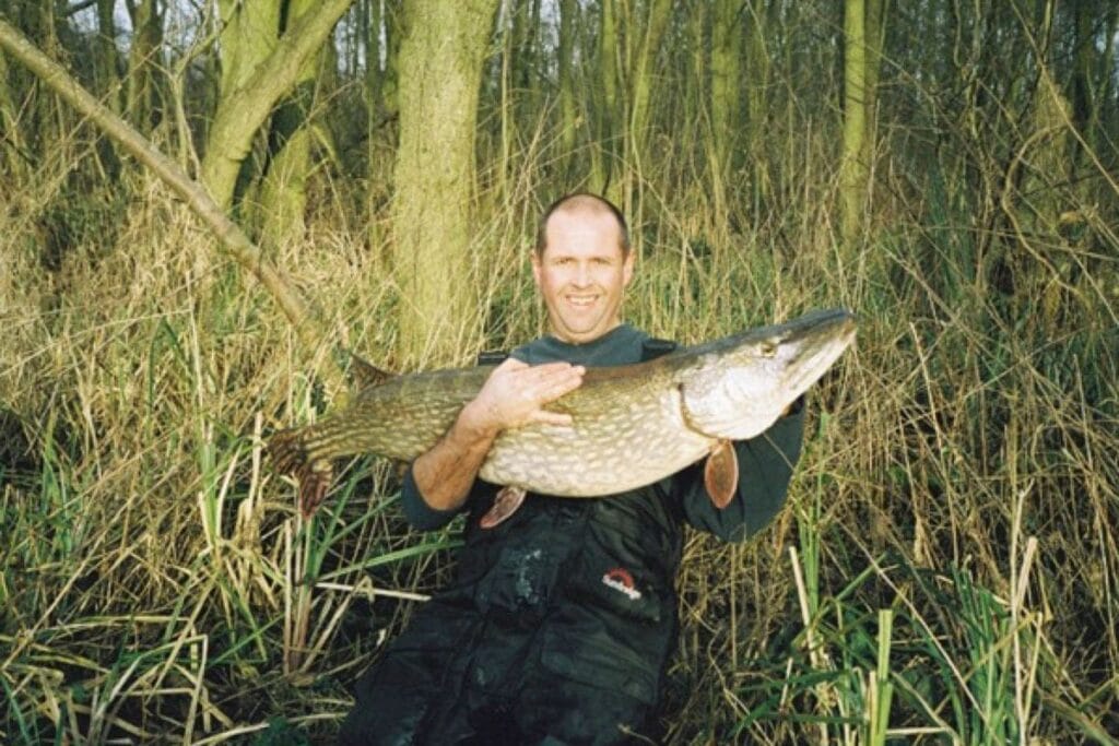Person holding large pike fish in woodland area.