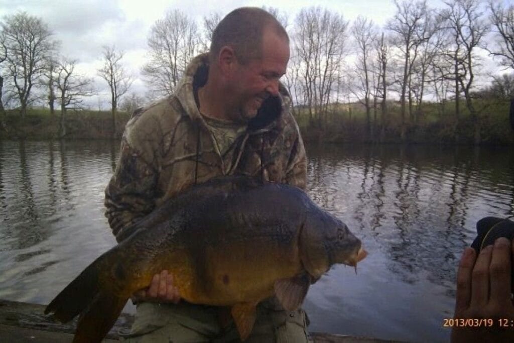 Man holding large fish by a riverbank.