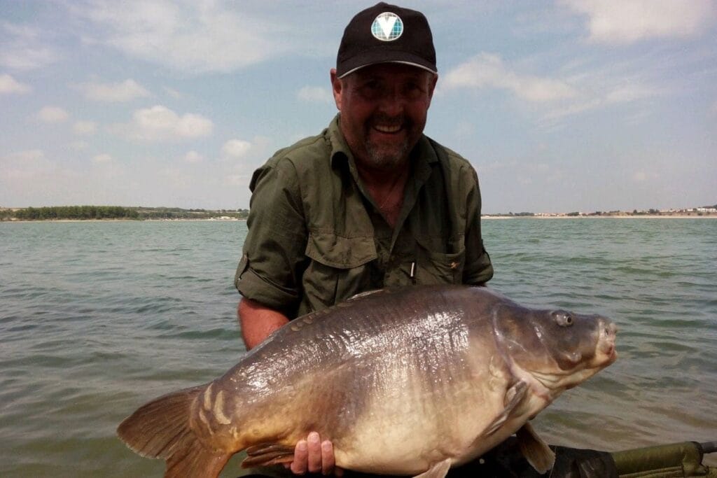 Smiling man holding large fish by the lake.
