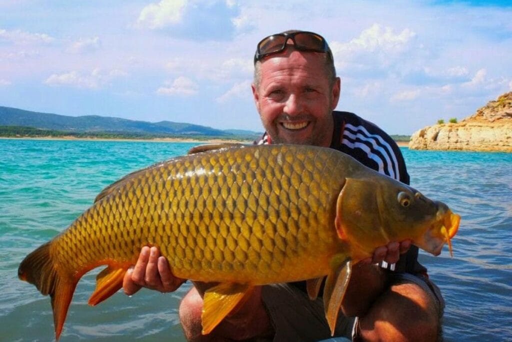 Person holding large carp by the water