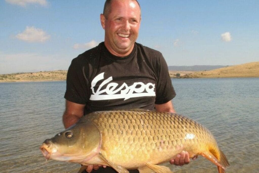 Man holding large fish by lake.