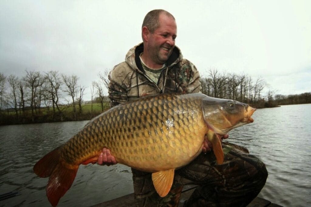 Fisherman holding large carp by the lake.