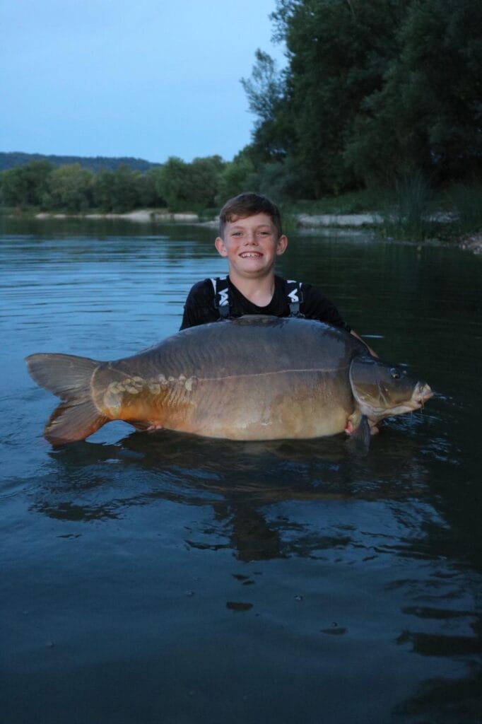 Smiling boy holding large fish in river.