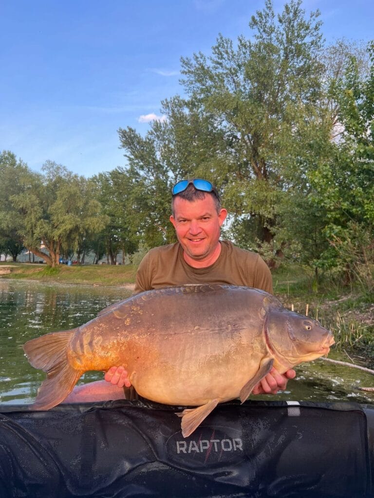 Man holding large carp by a lake.