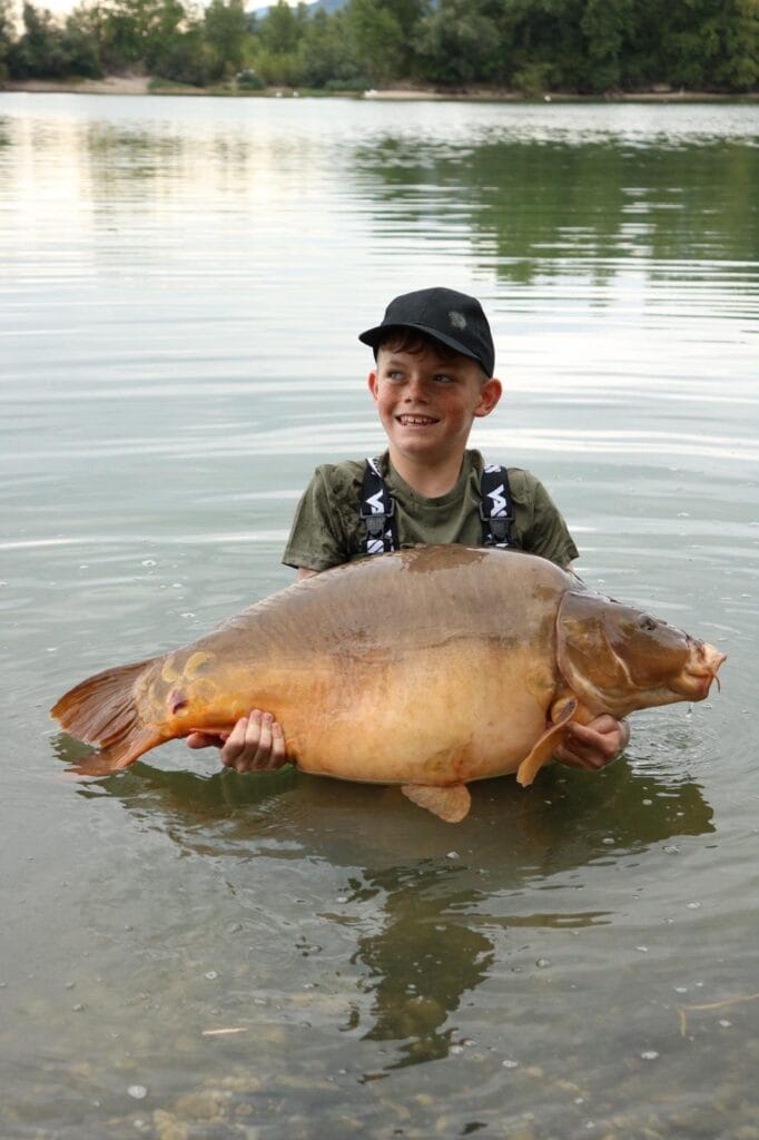 Boy holding large fish in lake.