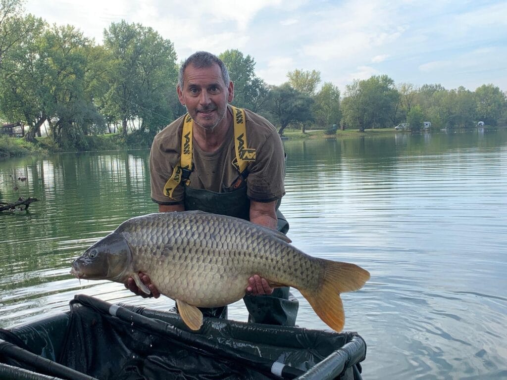 Man holding large fish by lake.