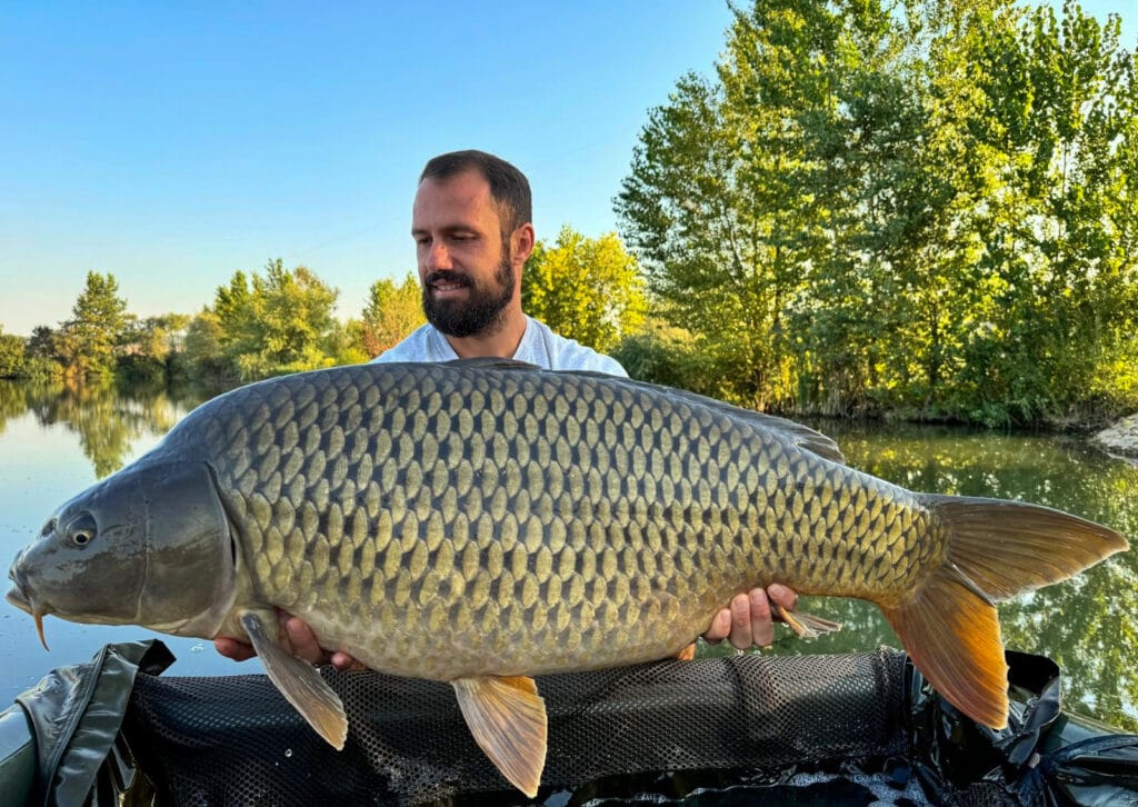 Man holding large carp by a lake