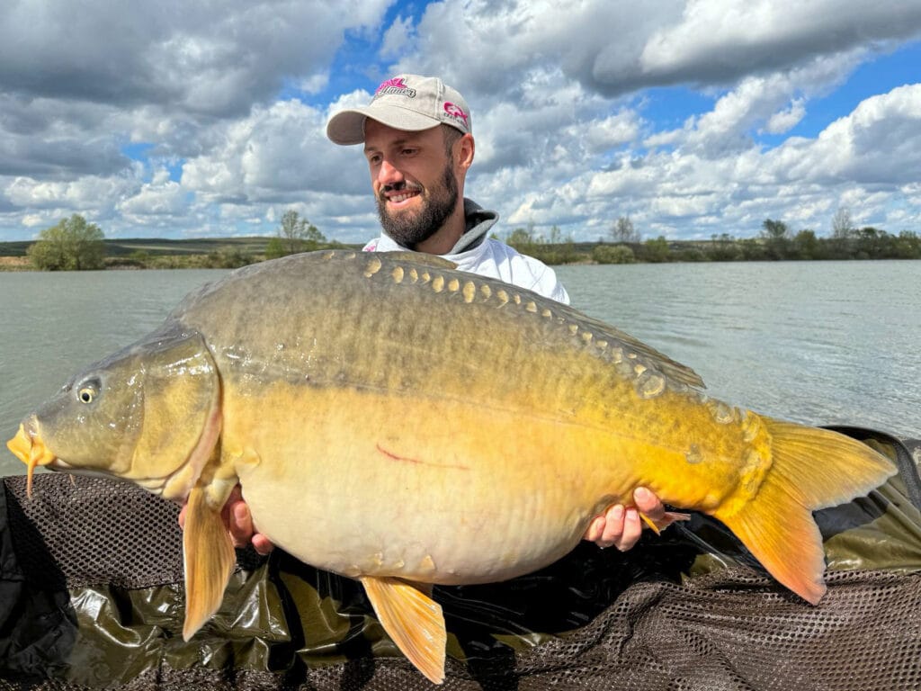 Man holding large carp by a lake.