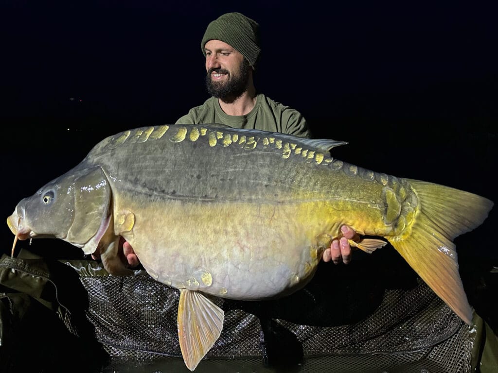 Person holding large carp fish at night.
