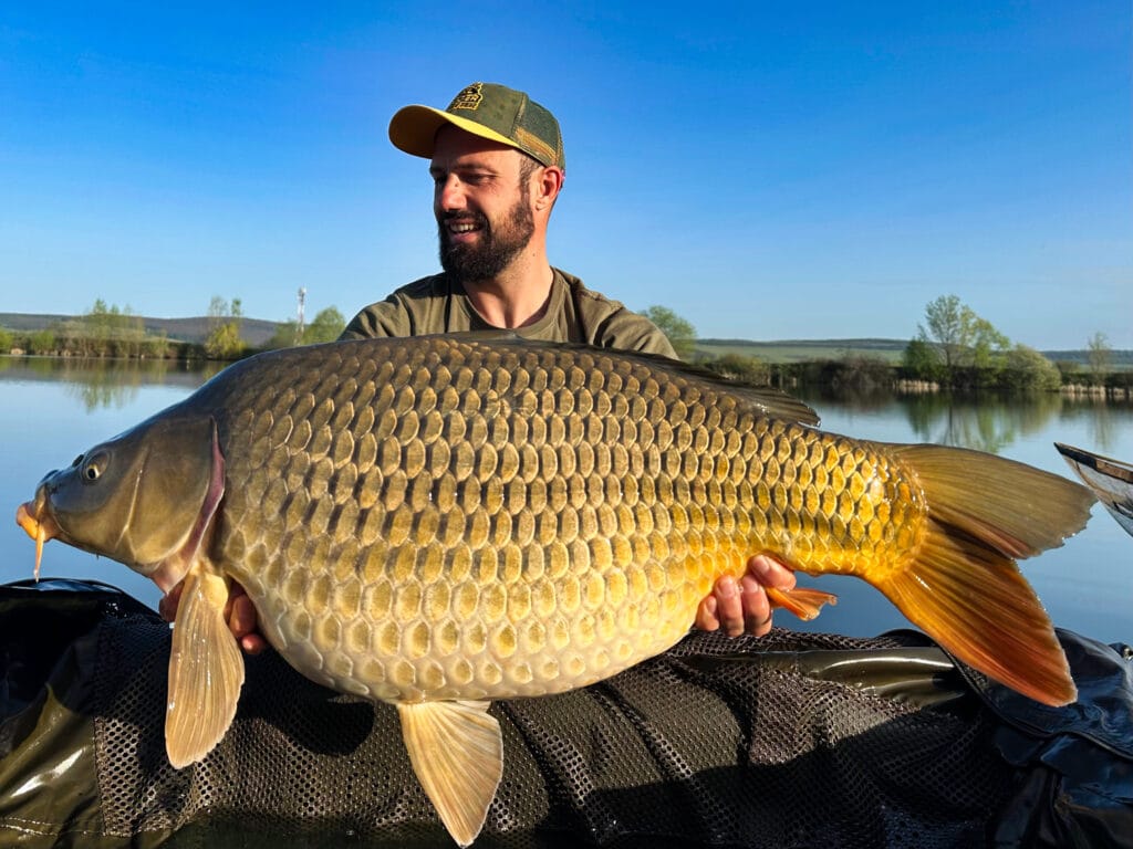 Man holding large fish by a lake.