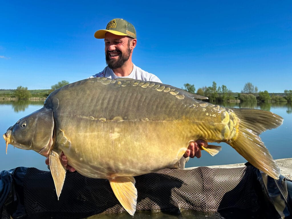 Man holding large carp by a lake.