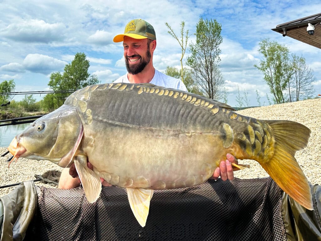 Man holding large carp by lakeside.