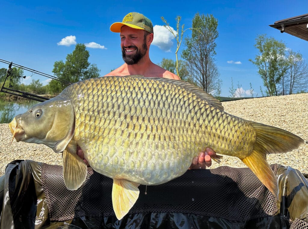 Man holding large carp by a lake.