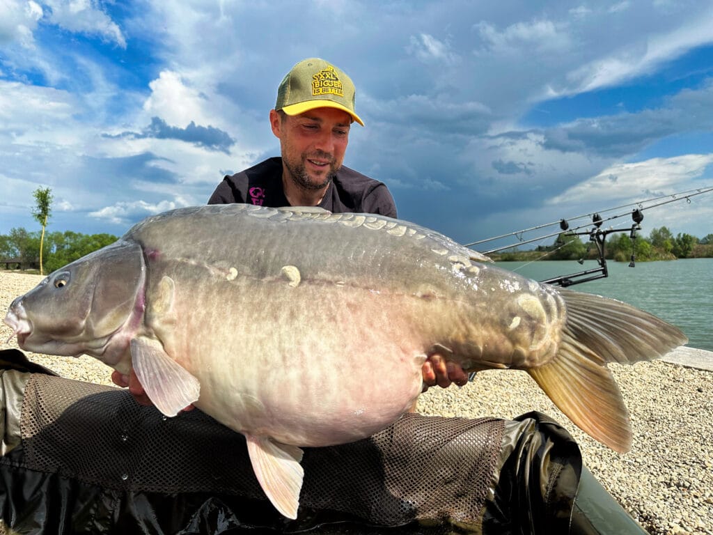 Man holding large fish by a lake.