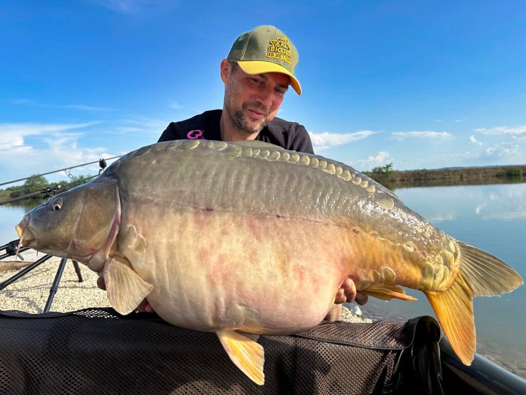 Man holding large carp by a lake.