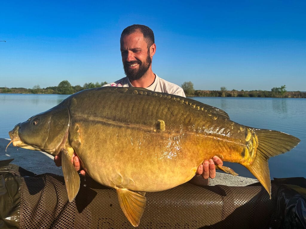 Man holding large carp by a lake.
