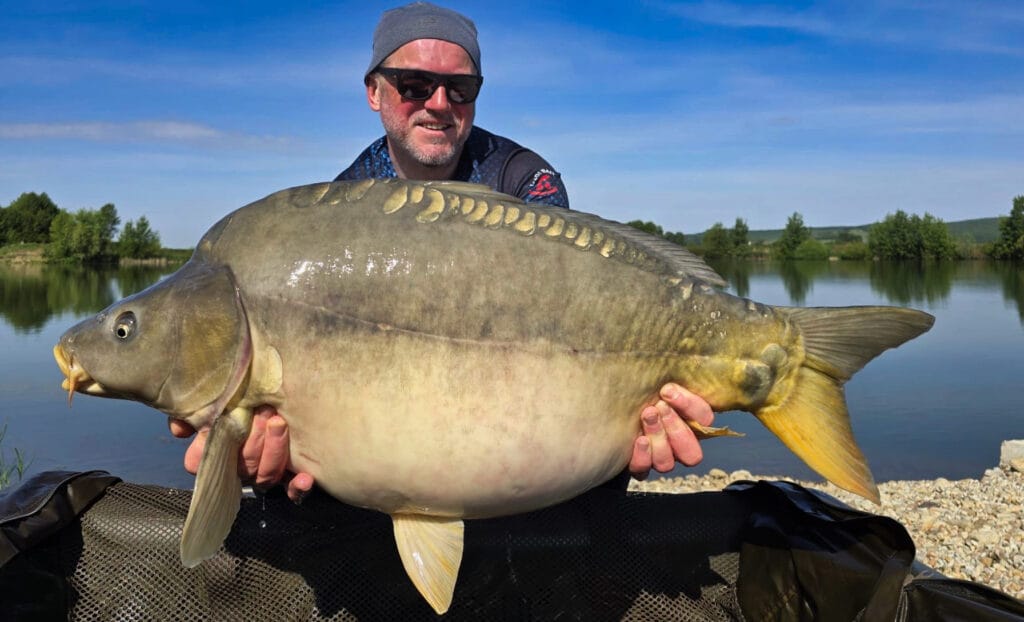 Angler holding large carp by the lake.