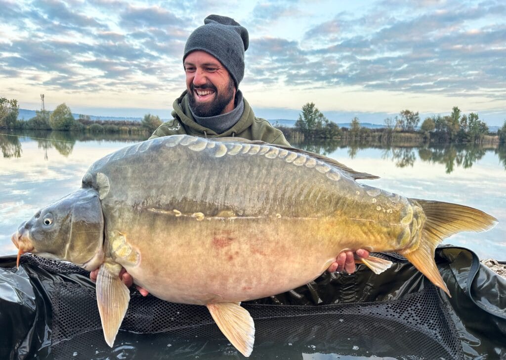 Man holding large carp by scenic lake.