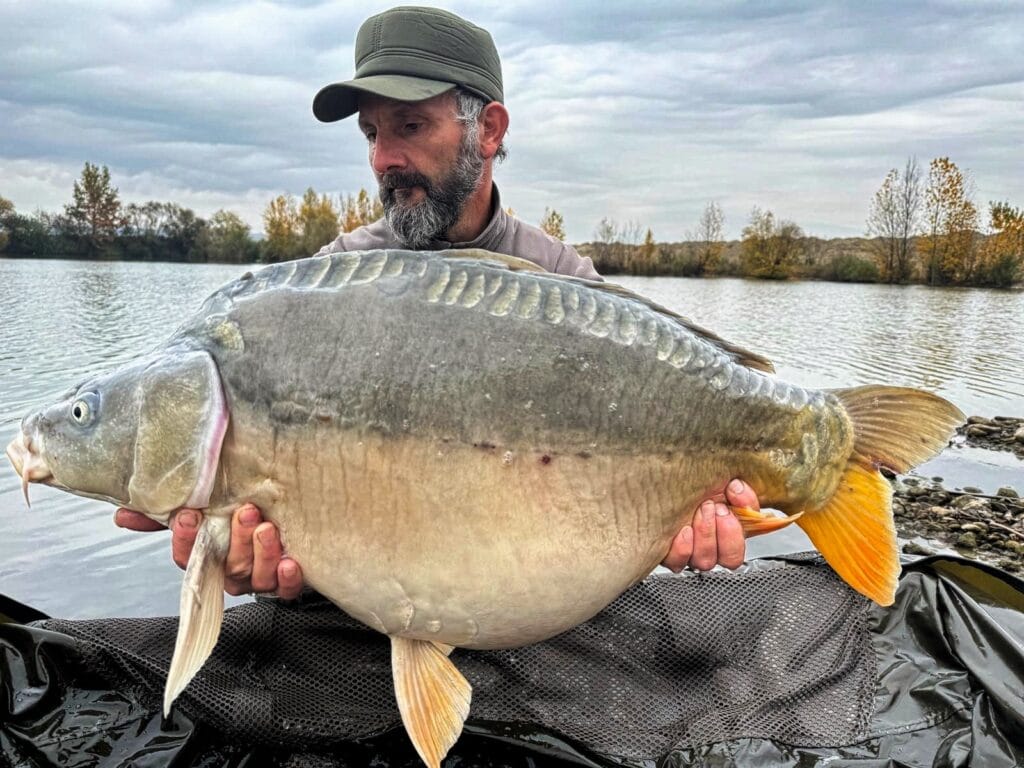 Man holding large fish by a lake.
