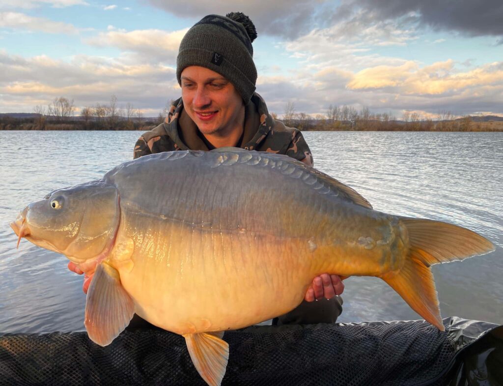 Person holding a large carp by the lake.