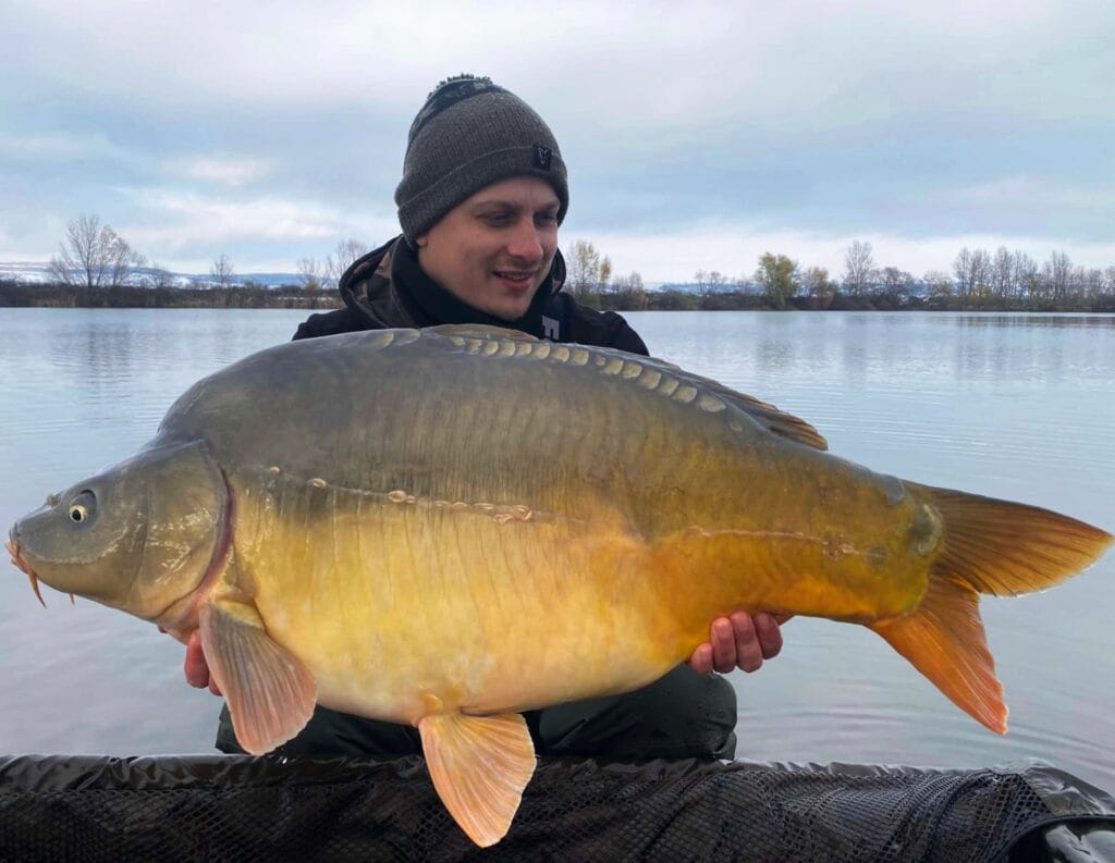 Person holding large carp by a lake.