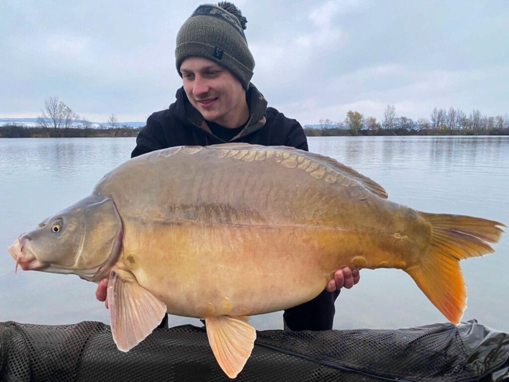 Man holding large carp near lake.