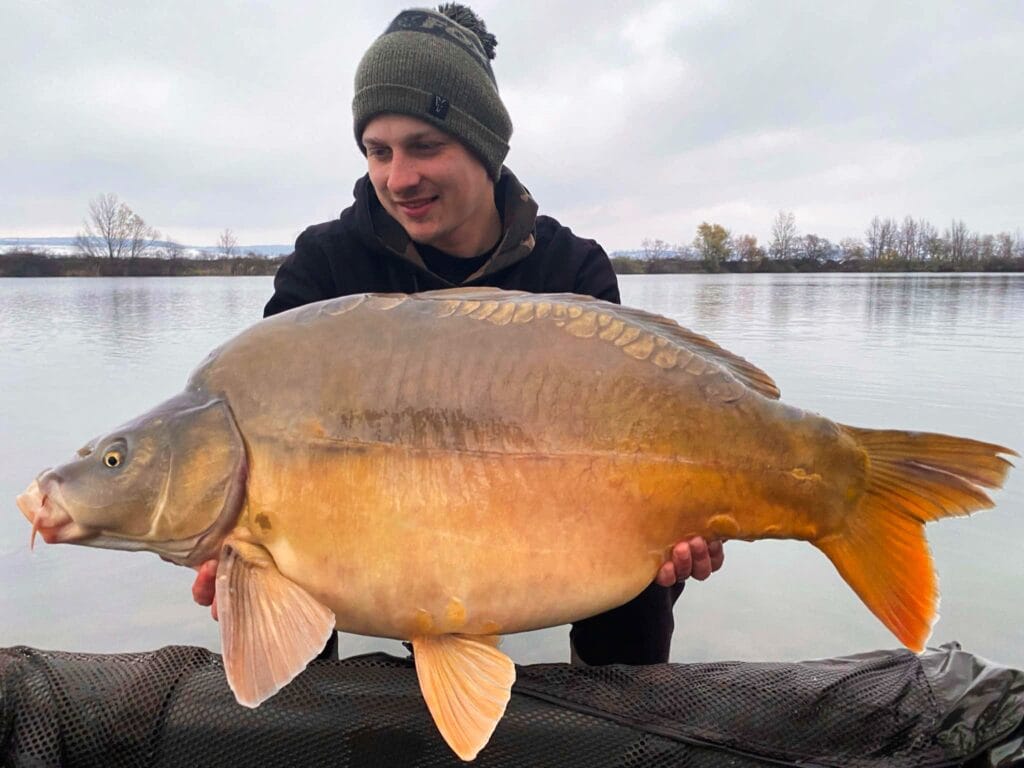 Person holding a large carp by the lake.