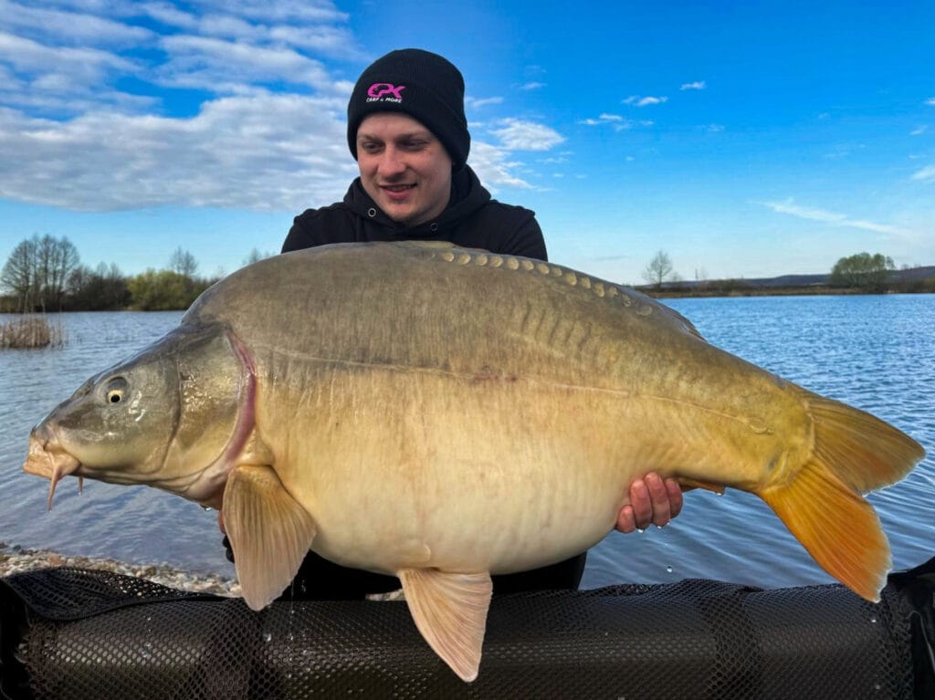 Angler holding a large carp beside the lake.