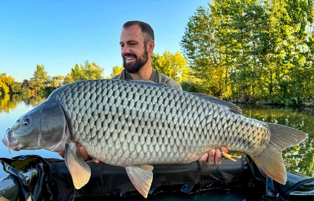 Man holding large fish by lakeside.