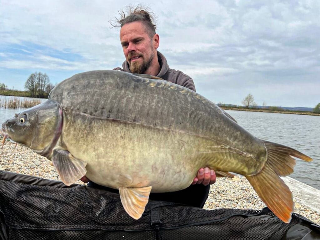 Man holding large carp by the lake.