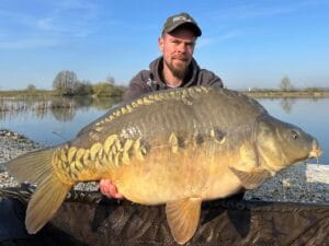 Angler holding large carp by lake.