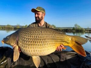 Man holding large carp by a lake.